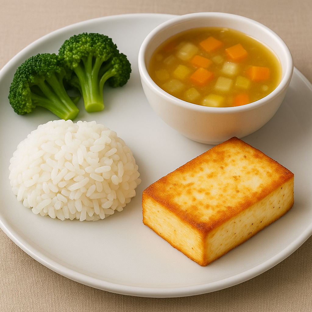 A plate with steamed white rice, broccoli florets, golden-brown paneer, and a bowl of clear vegetable soup.